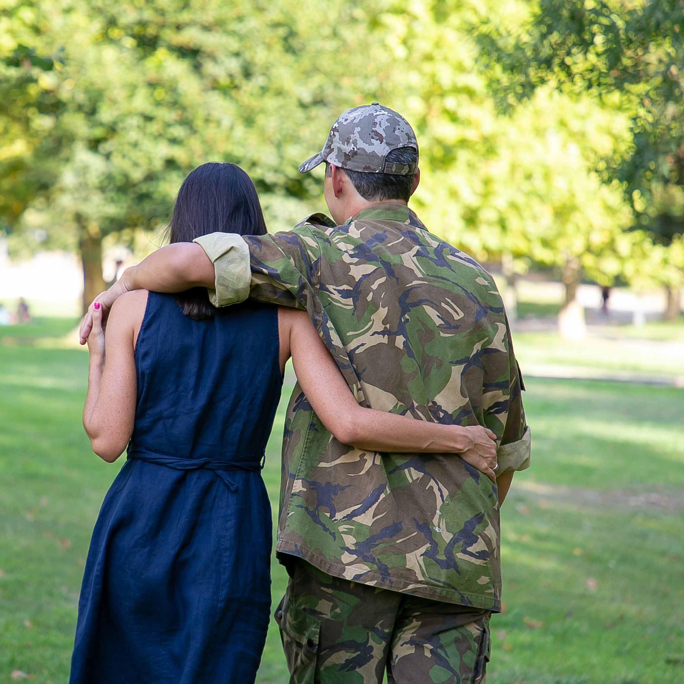 A man in the military walking with his arm around a woman.